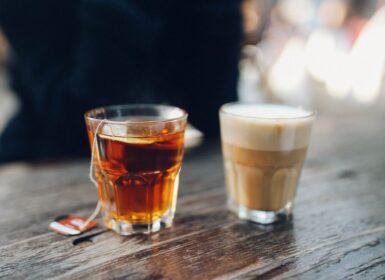Két pohár fekszik egy fából készült asztalon: az egyik teával, a teafilterből nyugtató Teint enged, a másikba habos, koffeinben gazdag kávét töltenek.