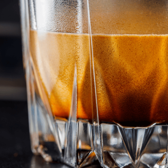 A glass of coffee with a brown liquid in it.